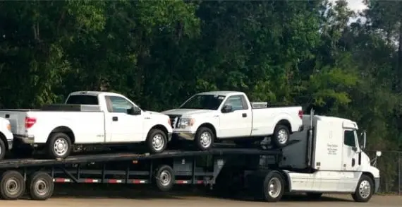 A truck is carrying three trucks on the back of it.